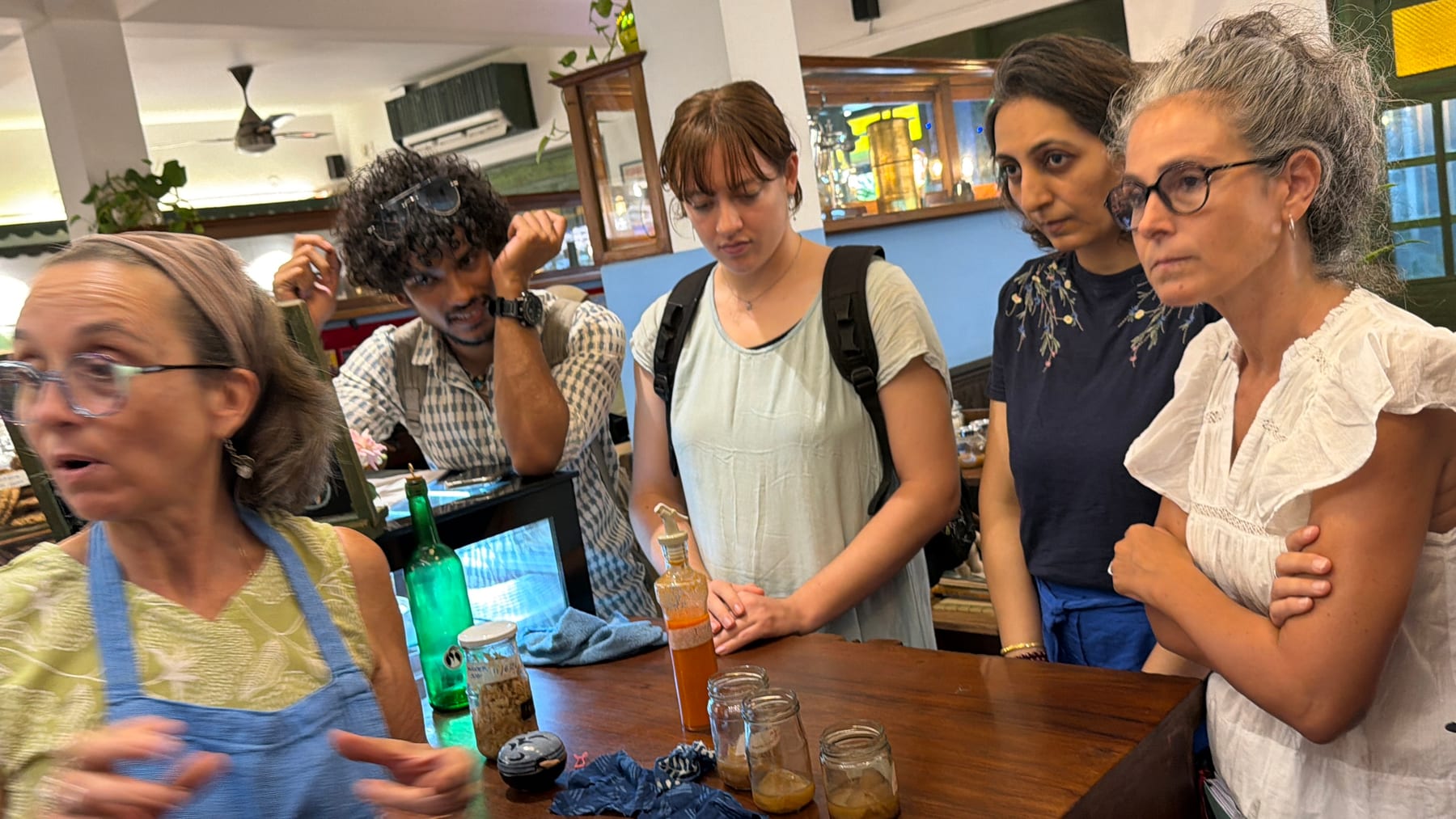 Matilda talking the fermentation class through a bottle of ferment as everyone gathers at the table